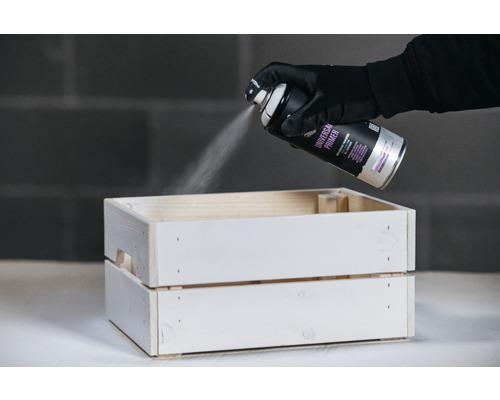 Eine Person sprüht mit Universalprimer eine Holzkiste.