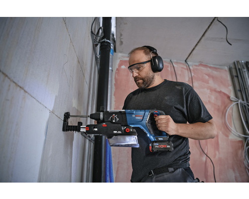 Handwerker mit Schutzbrille und Gehörschutz bohrt mit einem Bohrhammer ein Loch in eine Wand.