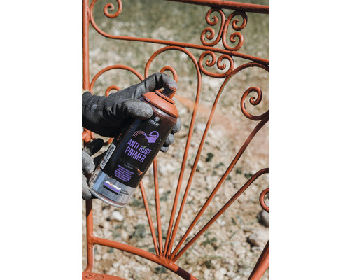 Eine Person sprüht mit einer Anti-Rost Grundierung ein Metallgitter