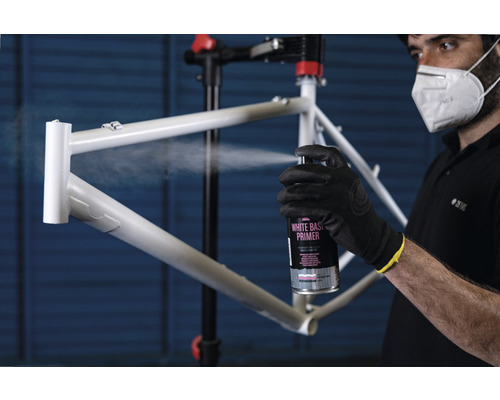 Eine Person grundiert einen Fahrradrahmen mit einer weißen Grundierungsspraydose.