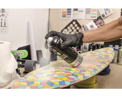 Eine Person trägt Handschuhe und sprüht Acryllack auf ein Skateboard.