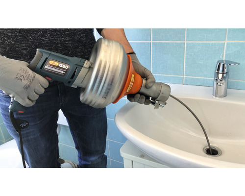 Person verwendet eine elektrische Rohrreinigungsspirale im Waschbecken, um eine Verstopfung zu lösen.