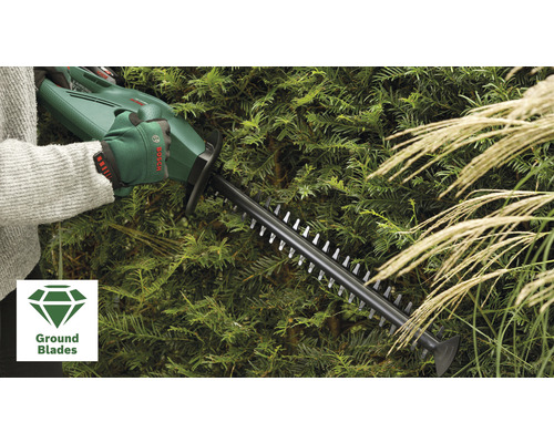 Eine Person bedient eine Heckenschere beim Schneiden einer Hecke. Im Vordergrund befindet sich das Ground Blades Symbol.