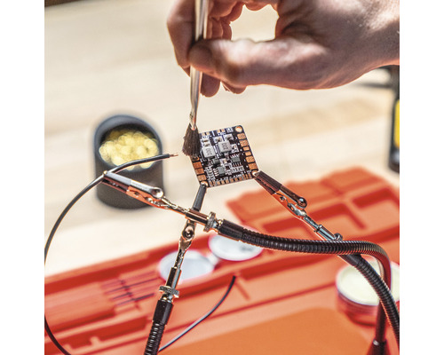 Elektronikplatine wird mit Pinsel gereinigt, fixiert mit Krokodilklemmen.