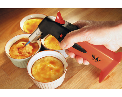 Eine Hand karamellisiert mit einem Brenner eine Crème brûlée.