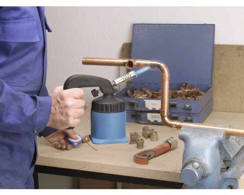Handwerker lötet Kupferrohre mit einem Lötbrenner, Rohrzange und Kupferfittings auf einer Werkbank