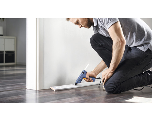 Mann befestigt Sockelleiste mit Heißklebepistole