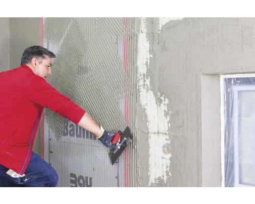 Ein Mann trägt Putz auf eine Wand mit Baumit Logo auf.