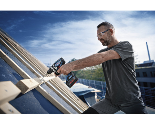 Ein Mann arbeitet mit einem Akku-Bohrschrauber auf einem Dach.