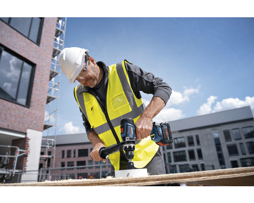 Ein Bauarbeiter bohrt mit einer Akku-Bohrmaschine ein Loch in ein Holzbrett.
