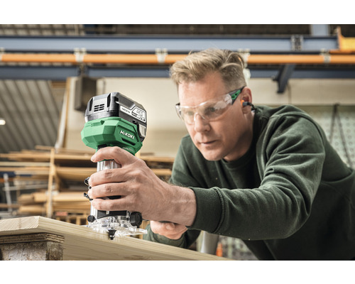 Mann verwendet Oberfräse an Holzbrett. Hikoki Logo.