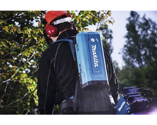 Eine Person trägt einen Makita-Akku-Rucksack mit einem Schutzhelm und Gehörschutz vor einem Baum.