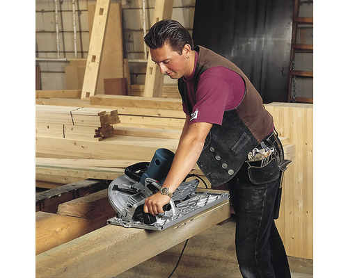 Ein Mann sägt einen Holzbalken mit einer Handkreissäge in einer Werkstatt.
