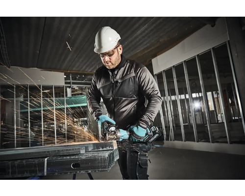 Mann mit Schutzhelm und Schutzbrille beim Schneiden von Metall mit einem Winkelschleifer in einer Baustelle