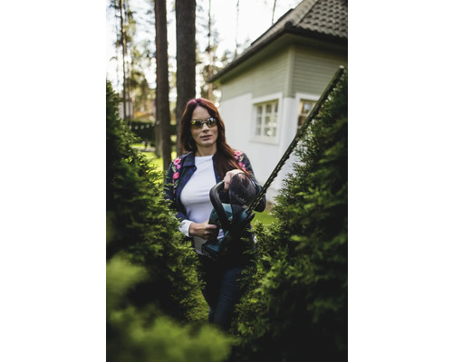 Frau schneidet Hecke mit einer Heckenschere im Garten.