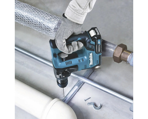 Eine Hand hält einen Akku-Bohrhammer der Marke Makita beim Bohren eines Lochs in ein Metallrohr.