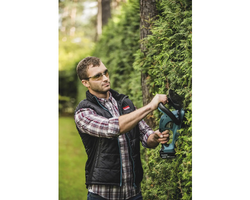 Ein Mann schneidet eine Hecke mit einer Akku-Heckenschere von Makita.