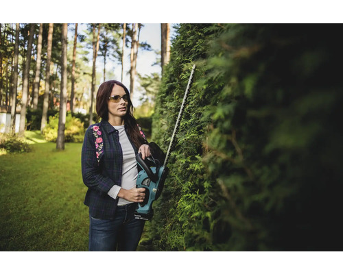Frau schneidet Hecke mit einer Heckenschere im Garten.