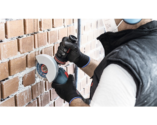 Handwerker schneidet mit einem Winkelschleifer eine Ziegelwand