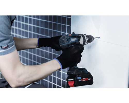 Eine Person bohrt mit einer Bohrmaschine ein Loch in eine Wand.