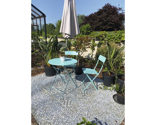 Gartenszene mit Bistroset, Sonnenschirm und Kübelpflanzen auf Kiesfläche