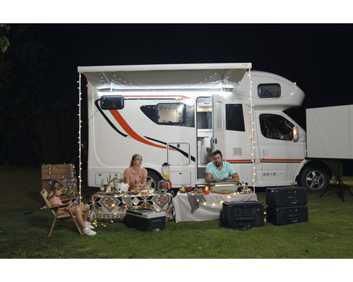 Familie genießt Campingurlaub vor Wohnmobil mit Lichterketten und Solargenerator