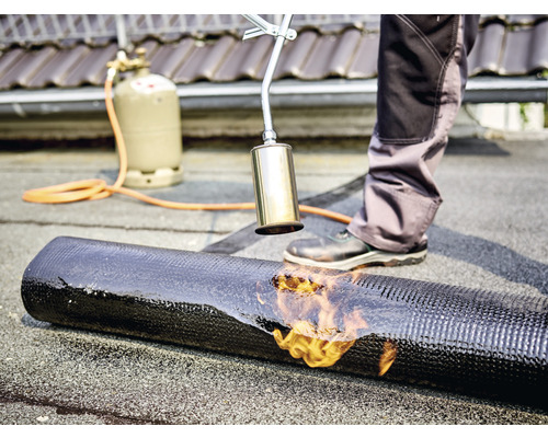 Ein Dachdecker schweißt eine Bitumenbahn mit einem Gasbrenner auf einem Dach.