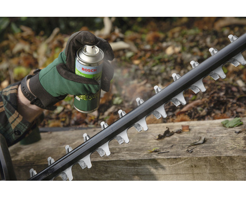 Eine Person sprüht mit einem Pflegespray von Bosch die Klinge einer Heckenschere ein.