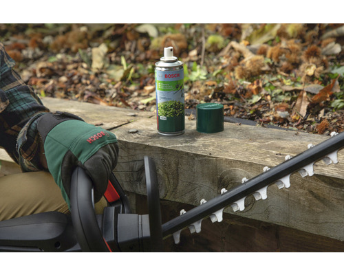 Bosch Logo. Person mit Gartenhandschuhen und Heckenschere neben einer Sprühdose für Heckenscherenpflege auf einer Holzoberfläche.