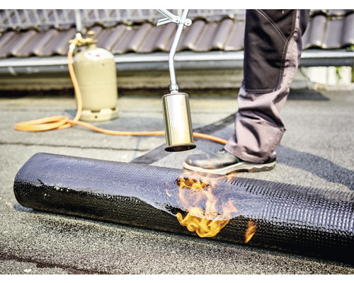 Dachdecker schweißt mit einem Gasbrenner eine Dachbahn auf ein Dach