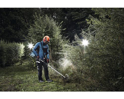 Mann mit Sicherheitsausrüstung und Akku-Rasentrimmer im Garten bei der Arbeit