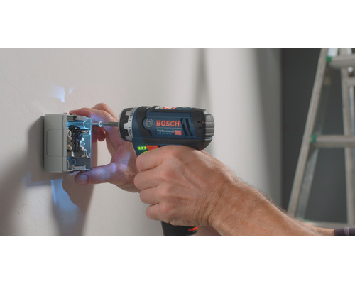 Elektriker befestigt Steckdose mit Akku-Bohrschrauber von Bosch an der Wand.