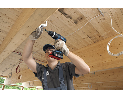 Handwerker montiert mit einem Akku-Bohrschrauber eine Halterung an einer Holzdecke.