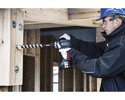 Ein Bauarbeiter bohrt mit einem Akku-Bohrschrauber ein Loch in einen Holzbalken.