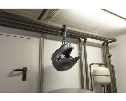 Ein Motocross-Helm hängt an einer Rohrschelle an einer Heizungsleitung.