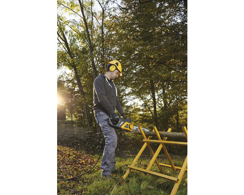 Mann sägt Holzscheit mit Elektrokettensäge auf einem Sägebock im Garten