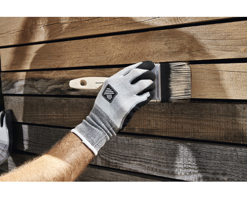 Eine Person trägt Handschuhe und streicht Holz mit einem Pinsel.