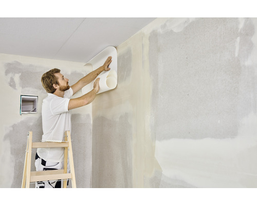 Mann tapeziert eine Wand mit einer Tapetenrolle auf einer Leiter