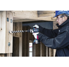 Handwerker bohrt mit einem Akku-Bohrschrauber ein Loch in einen Holzbalken.