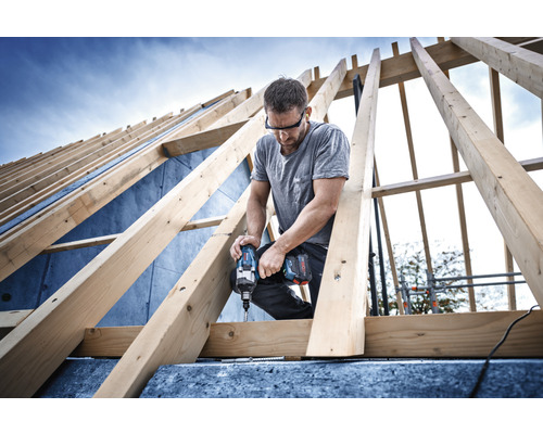 Handwerker arbeitet mit einem Akku-Schlagschrauber an einem Dachstuhl aus Holz.