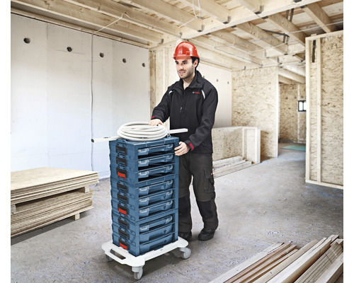 Handwerker schiebt einen Werkzeugwagen mit mehreren Schubladen in einem Rohbau.