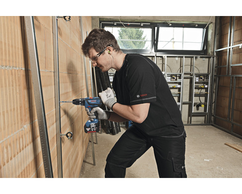 Ein Mann bohrt mit einer Bohrmaschine ein Loch in eine Wand auf einer Baustelle.