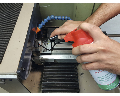 Eine Person sprüht Reiniger auf eine Werkzeugmaschine zur Reinigung.