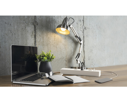 Arbeitsplatz mit Schreibtischlampe, Laptop und Steckdosenleiste auf einem Schreibtisch.