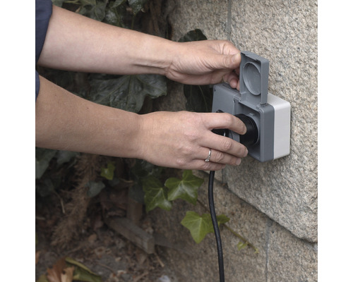 Person steckt Stecker in eine wassergeschützte Außensteckdose