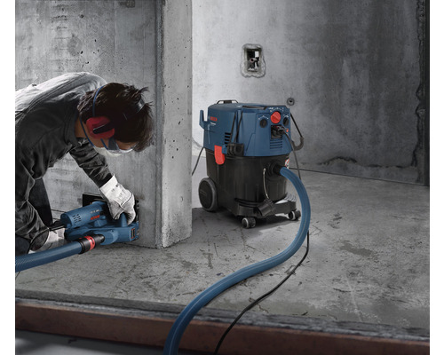 Mann arbeitet mit einer Mauernutfräse und einem Industriestaubsauger von Bosch an einer Betonwand.