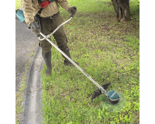 Eine Person benutzt einen Freischneider im Garten, um Gras zu schneiden.