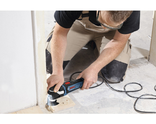 Handwerker bei der Arbeit mit einem Multifunktionswerkzeug von Bosch an einer Holzleiste in einem unfertigen Raum.