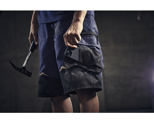 Mann mit Zimmermannskluftshorts, Handy in der Tasche und Hammer in der Hand