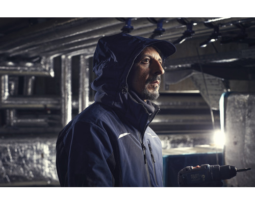 Ein Handwerker mit Jacke und Akkuschrauber arbeitet in einem Gebäude.